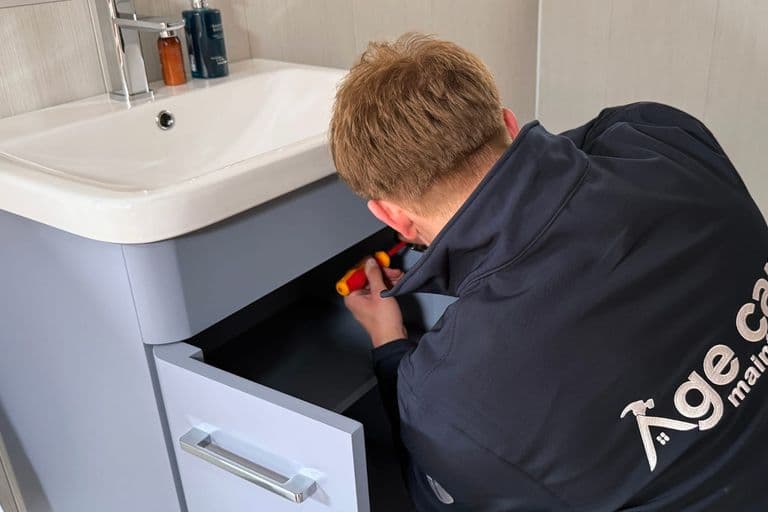 An Age Care Maintenance handyman working under a bathroom sink
