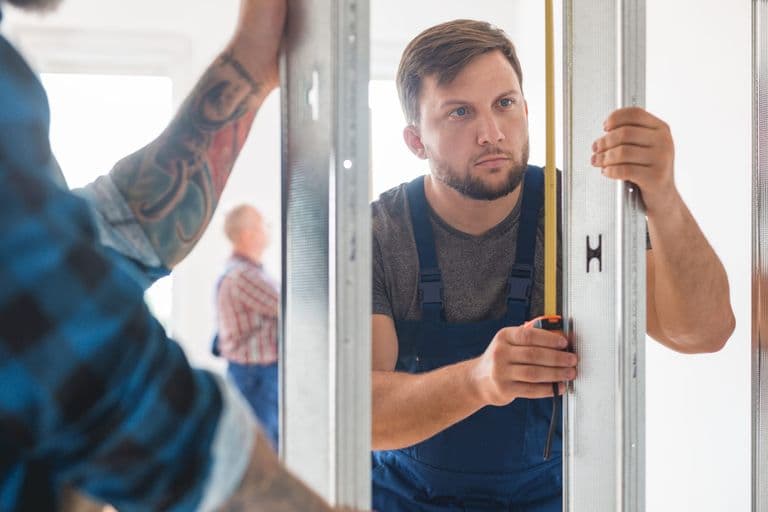 Two tradesmen measuring and fitting a new door frame