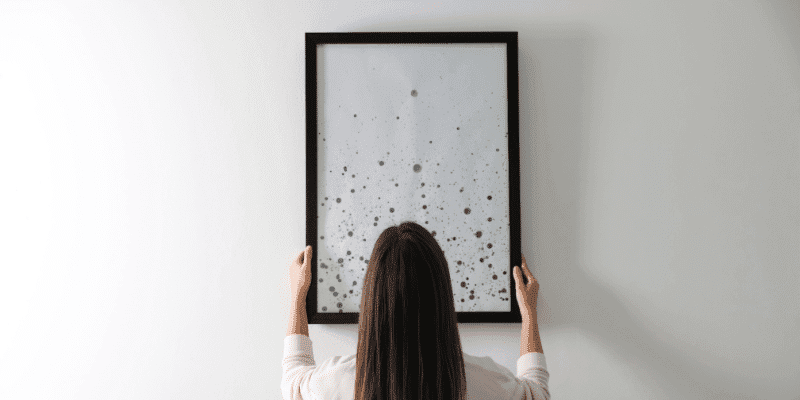 A woman hanging a framed picture on a wall
